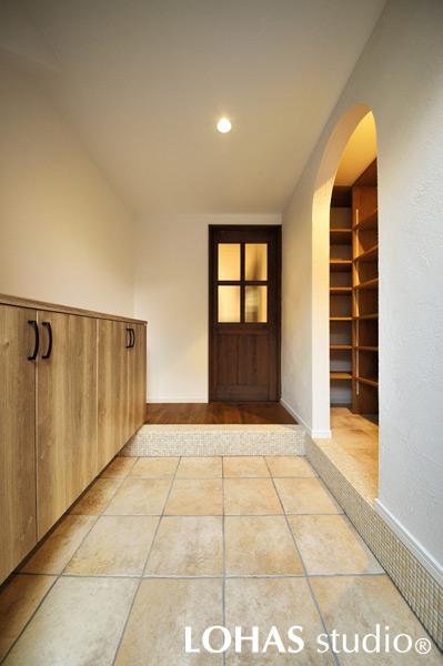 ベビーカーでも楽々入るシュークロークを具えた玄関です。品のある大判タイルを敷きました。アーチの開口から入った先には物入れを造作。可動棚なので靴以外の収納もOKです。