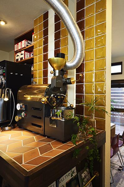 からし色や茶色など、渋めの色のタイルをミッドセンチュリー調に貼り合わせた印象的な壁と、レンガタイルを天板に使った造作の焙煎カウンター。焙煎機2台を同時に動かせるよう使い勝手よく、メンテナンスしやすく、さらに入口から見えやすいようになっている。