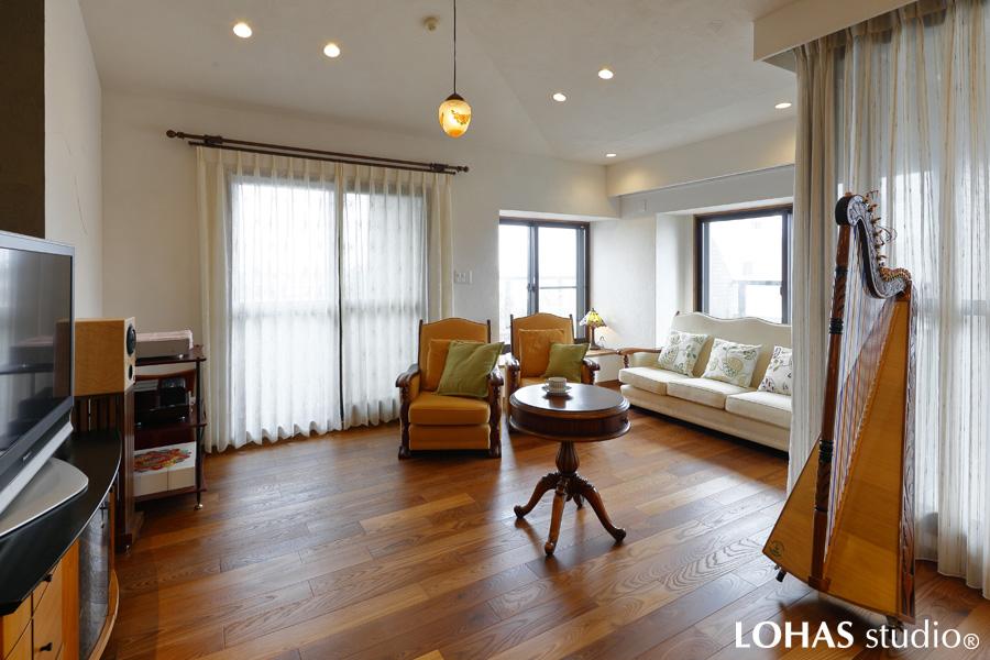 2方向から光の降りそそぐ明るいリビングです。床には渋みのある色味が特徴的なアッシュのフローリングを施工。お手持ちの家具や奥さまのアルパと見事に調和しています。天井には複数の間接照明をご用意し、雰囲気たっぷりの中で映画鑑賞を楽しむことができます。