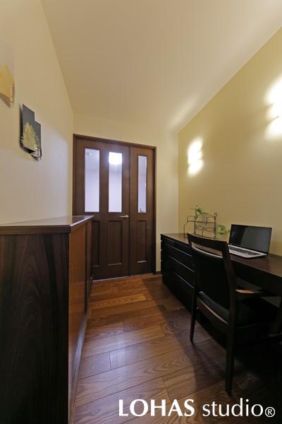 ダークブラウンの木目で統一されたワークスペースです。通り抜けられるようなつくりになっており、玄関から入って奥さまの寝室へと繋がっています。重厚感のある落ち着いた色味が、作業に集中できる環境を作りあげています。