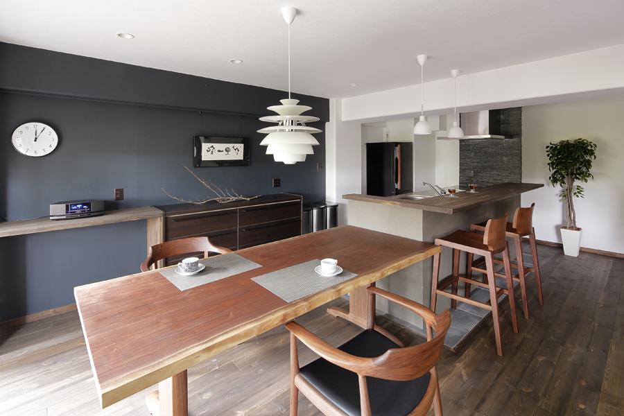 マニッシュなアクセント壁を眺めるダイニングです。フローリングは無垢パイン材をダークブラウン色に。照明が入るとロマンティックな景色に変わるキッチンカウンターは床と揃えてパイン材で造作しました。