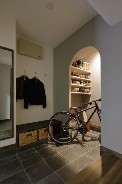 姿見やコート掛けを具えた使いやすい玄関です。玄関扉から見えない配置で自転車も入る大型のシューズクロークを造作しました。土間には手割りのような目地で表情豊かなタイル材を施工。