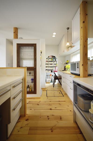 キッチンに併設された収納コーナーです。つきあたりに土間付きのパントリーを新設しました。勝手口とキッチンを直結しながら下がり壁でゆるく区切り ゲストから見えないように配慮。キッチンから離れた室内ゴミ置き場も兼ねて衛生的です。袖壁にはグラスや酒類を飾れる木製のガラス収納棚を造作しました。