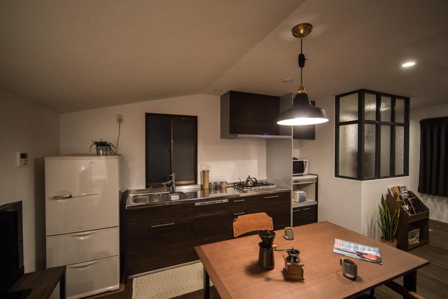 シックな雰囲気のI型キッチンです。ブラウンを主体にした落ち着きある装い。隣接する玄関との間に内窓付きの間仕切りを設けました。背低い海外風の冷蔵庫やペンダント照明で斜めの天井フォルムがセンス良く映えています。