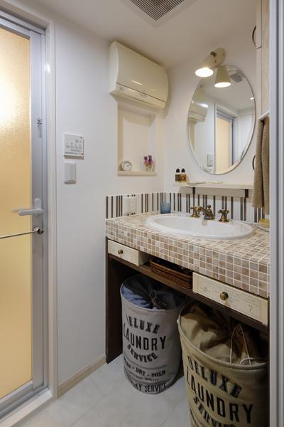 モザイクタイルが可愛らしい洗面室です。石のような見映えの床はメンテナンス性の良いフロアタイル。カウンターはストライプのタイルでスパイスを効かせスタイリッシュな雰囲気に。オリジナルの引き出しが個性を出しています。