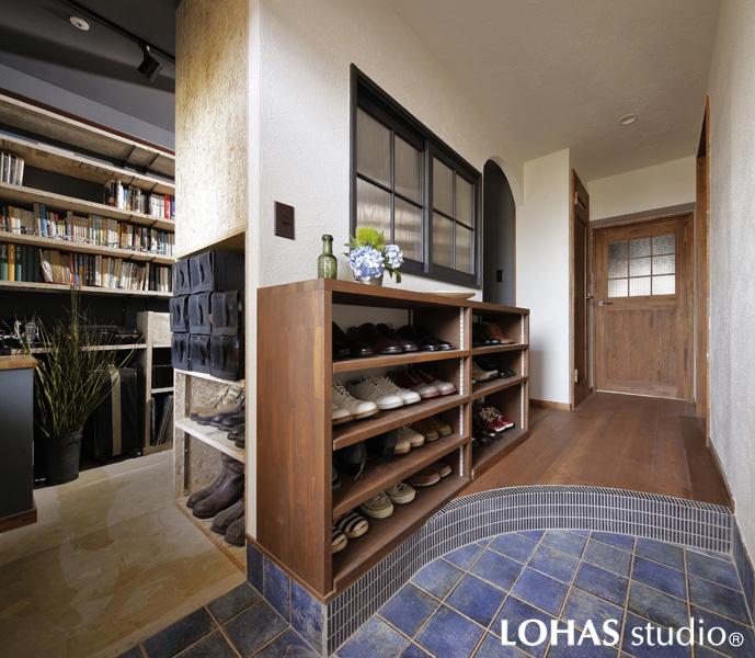 ブルーのタイルが印象的な明るい玄関です。土間から続く横長のシューズボックスを造作して収納力を強化。趣味室側にもニッチを使った収納を追加しています。以前は「狭く」感じていた室内が 室内窓の効果で広く感じるように。