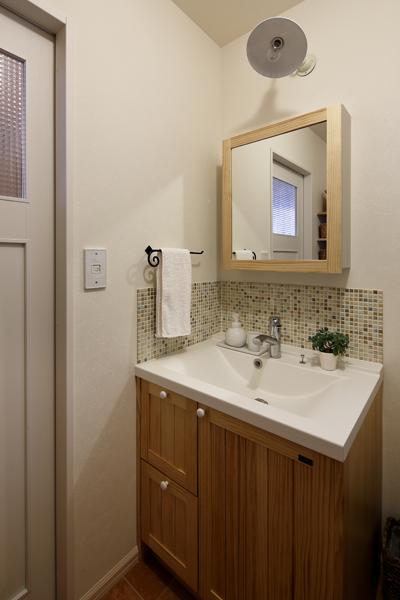 白壁にモザイクタイルが映える爽やかな洗面室です。水彩ようにの色のにじんだタイルが透明感をプラス。かぎ状に設えた動線の片側はキッチン、他方は廊下につながり1階を一周できる回遊動線の一部になりました。水まわりがつながる動線で家事ラクを後押し。