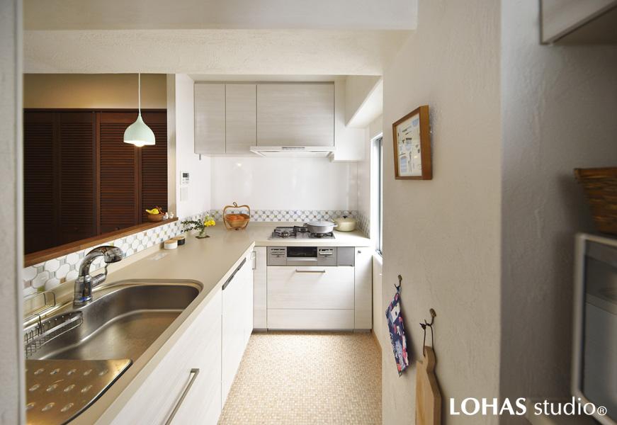 調理場を経由して外出/帰宅していた動線を改めL字型に配置を変えたキッチンです。玄関方向にヌケがあるため開放的な室内観。腰壁で通路から中が丸見えにならないよう工夫されています。色合いは白基調のさっぱりと清潔な装い。透明感のあるタイルでシンク周りを軽やかに縁取っています。