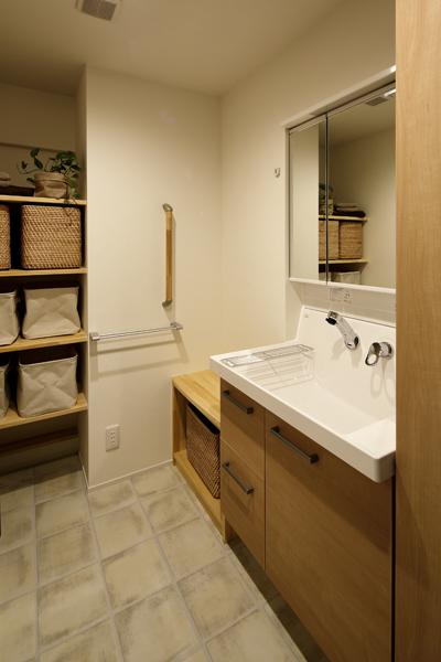 木目調で優しい雰囲気の洗面室です。タイル調の床は泥汚れにも強いPタイル。天井には珪藻土を施工。固定棚やベンチを肌さわりの良いパイン材で造作しています。車椅子でも入れるよう通路は広くご用意。