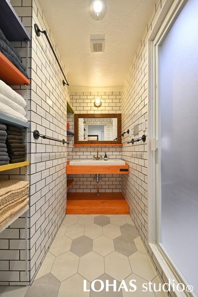 鮮やかなオレンジ色が目を惹く洗面スペースです。水回りは壁と床のタイルを統一し、ホワイトとグレーに絞り込むことで差し色が一層映えるデザインにしています。