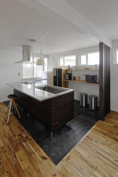 アイランドタイプのシックなキッチンです。カウンターはナラ材でオリジナルを制作。同じ素材で壁側にも棚を追加。使い込んだコンクリートのような粗い表情のタイルが敷かれ上質な雰囲気。