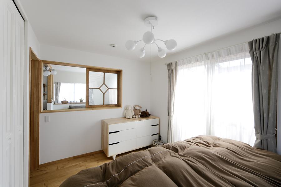 オリジナルで造作した室内窓のある寝室です。木枠とデザインガラスで可愛らしいインテリアが出来ました。窓の先にはリビングが繋がり 窓を開ければ広がりある室内観が作れます。隣接するベランダからの光や風は寝室を通ってリビングまで抜けるそう。