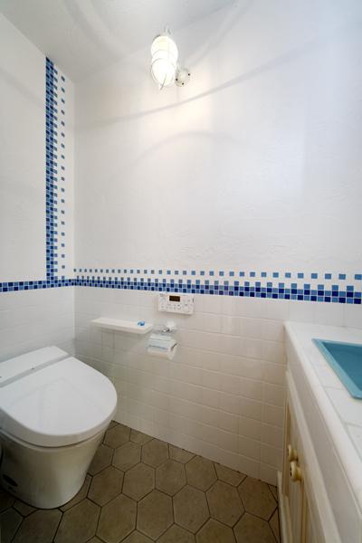 南欧風のタイルデザインを採り入れたトイレです。床の大人シックな六角タイルはフランスの伝統的な品。壁には腰まで白タイル、直線でブルーを挿し込んで艶のあるリッチな装いに。水栓や手洗いシンク 照明にもこだわり清涼なイメージです。