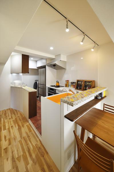 オレンジ色のシンクが可愛らしいオープンタイプのキッチンです。カウンターのタイルも柑橘系の軽やかな色合いに。家電収納はサイズを合わせて家具を造作。多目的なユーティリティースペースには洗濯機を設置しました。