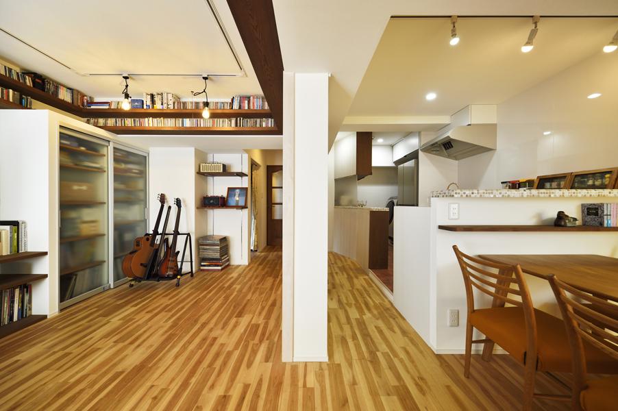 構造壁(中央)を残した左右でゆるやかに役割を分けるLDKです。既存の洋室＋LDKを同じ無垢カバザクラ材で床施工し統一感をもたせました。キッチンをオープンタイプに、照明をダクトレールにすることでスッキリした景観に。