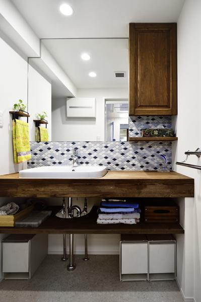 清涼感のあるタイルを施工した洗面室です。木製の吊収納と洗面台はオリジナルの造作家具で色合いをLDKと揃えています。壁面の壁は下がり天井のフォルムに合わせてカットしピッタリはめ込みました。