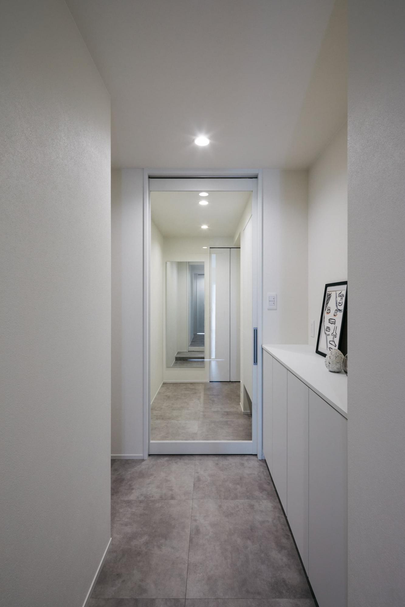 玄関と廊下の境には断熱のためにガラス建具を採用。玄関にも廊下やLDKと同一の床材を用いて、扉より50cmほど手前に段差を計画することにより廊下との繋がりが生まれています。