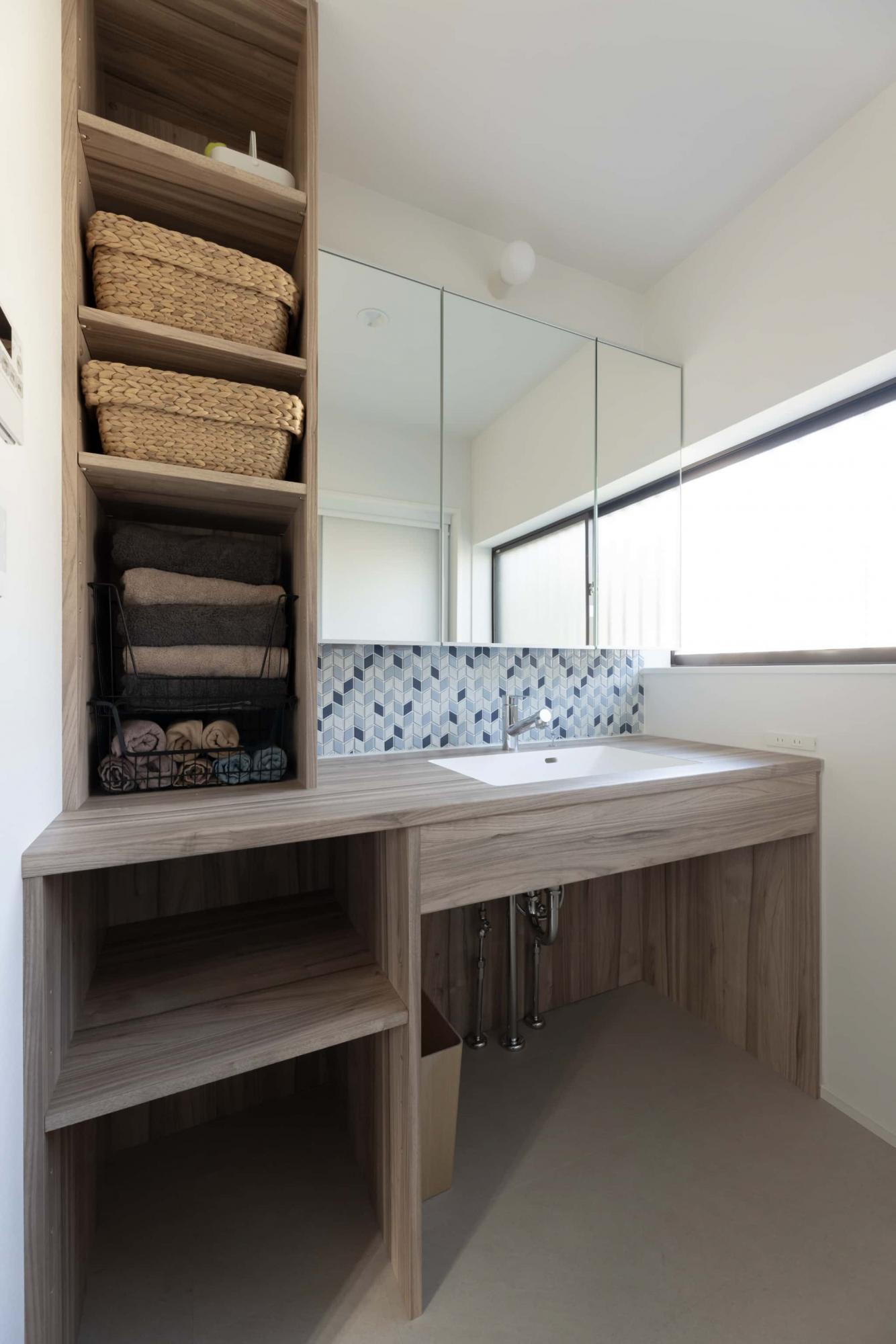 造作洗面台のカウンター天板と収納棚をグレーウッドで統一した明るく清潔感のある洗面脱衣所。ブルー系のひし形タイルがとても可愛らしく、アクセントに。