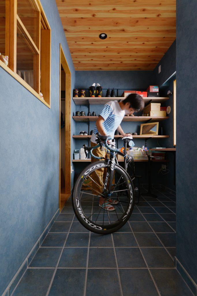 趣味の自転車を整備できる広々土間。色見にもこだわったタイル床。室内窓や靴収納は無垢材を採用。写真奥左側からウォークインクローゼットに繋がっている回遊スタイルです。