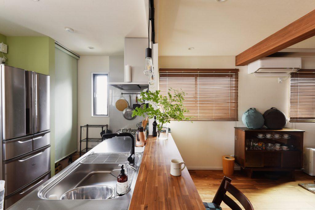 対面のオープンキッチンは集成材カウンターと木製ブラインド＋木目調クロスの梁でナチュラルな感じに。ステンレスと木の相性っていいんです！以前から大切に使ってきた茶箪笥も良くマッチしています。