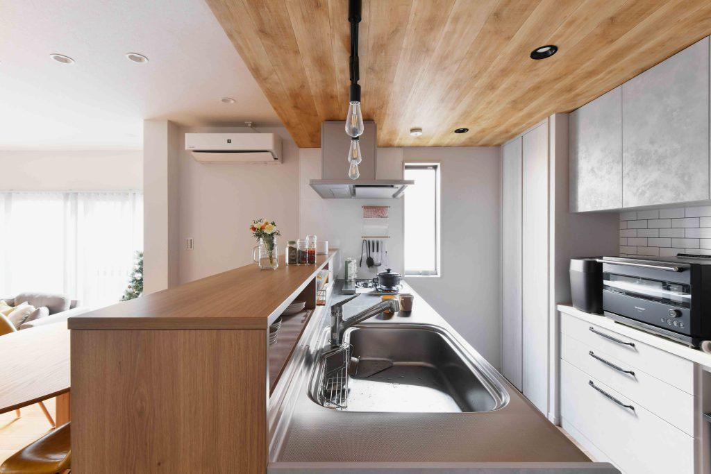 キッチン部分の下がり天井には木目のアクセントクロスを貼りました。ライティングレールやダウンライトは黒を採用して空間にメリハリをつけています。キッチパネルはマグネットがつくものを採用。キッチンツールの収納に大活躍です。