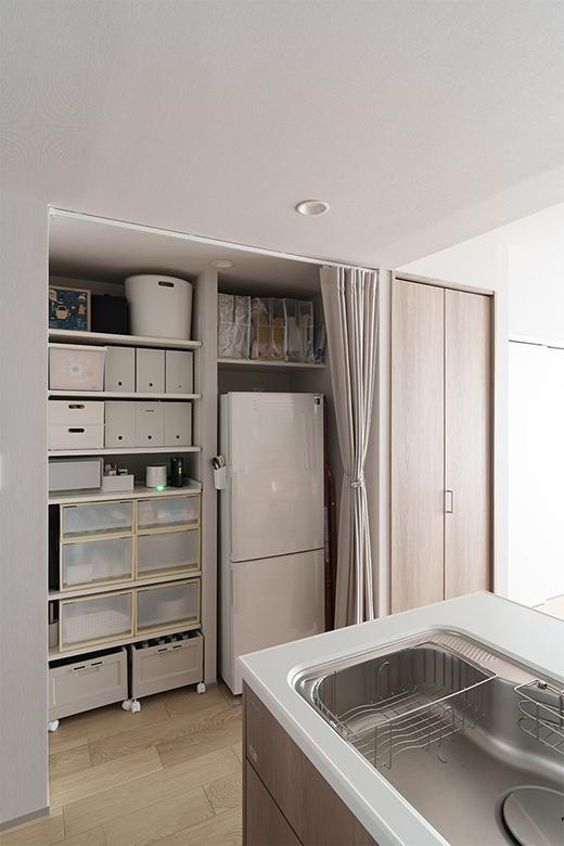 サブ冷蔵庫と脚立が収まるスペースを計算して造作棚の幅を決定したパントリー。圧迫感がなく、ふだんはカーテン仕切りを開けっ放しで使い、来客時はサッと隠せるように。大容量のパントリー収納がキッチンと近いので、片付けやすく使いやすいそうだ。