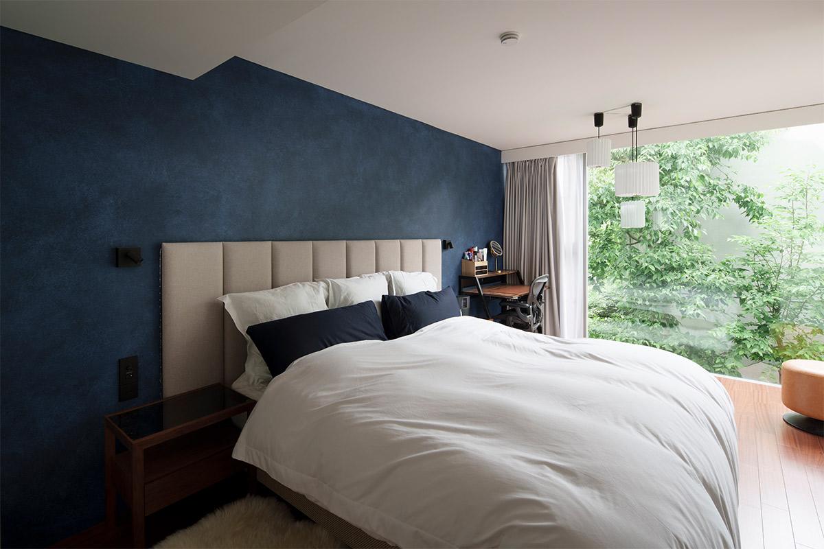 ネイビーのアクセントウォールは塗装仕上げ。窓外に広がるグリーンと融合し、ホテルの一室のようなゆったりくつろげるベッドルームに。間接照明の具体的なイメージはなかったので、建築士に提案してもらったという。