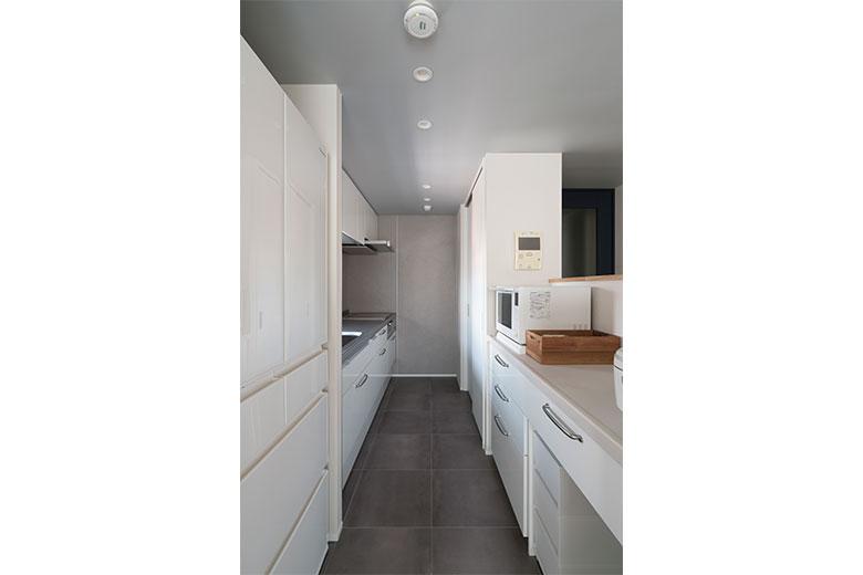 窓側にキッチンを置き、対面カウンターでリビングダイニングとつながるように。カウンターの壁の高さは、電子レンジが見えない高さとした。その隣の収納は、食器やパントリーとして使えるキッチン収納。