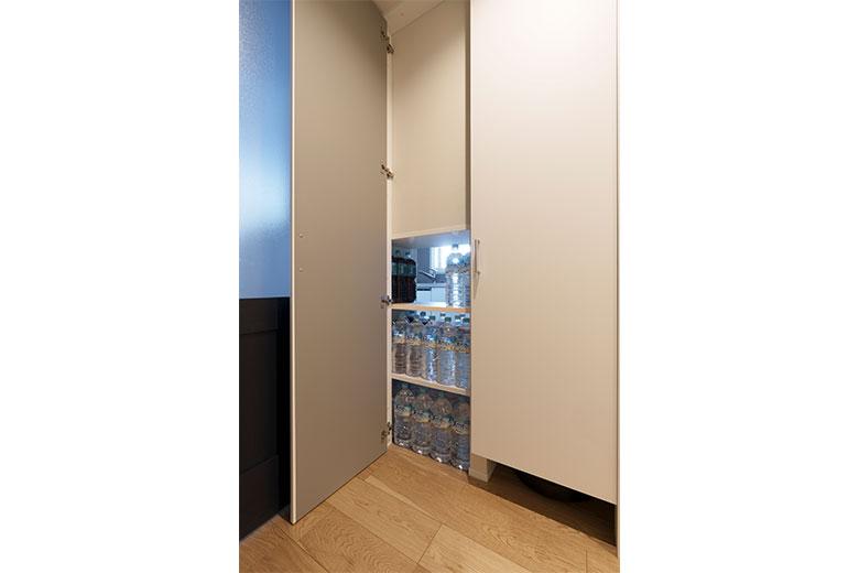 キッチン収納の下部は、廊下側からも出し入れが可能。防災備蓄として、水のペットボトル置き場となっている部分だが、玄関からぐるっと回って重いペットボトルの箱を運ぶのは大変そうだと話すと、建築士が廊下とキッチンの間の収納壁を抜くアイディアを出してくれたという。