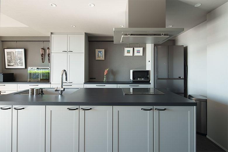 掃除のしやすさからオープンなアイランドキッチンに。さらに、家電もできるだけ収納したいので、収納力を上げるためにカップボードカウンターをダイニングまで壁一面に設けた。ピクチャーレールを付けたディスプレイカウンターを挟んだので圧迫感がなく、統一感があって美しい。