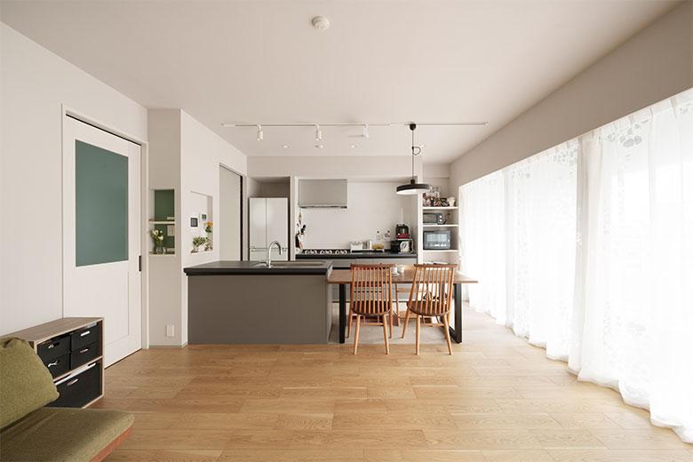 リビングのスペースを広く大きく取るため、キッチンを90度移動してダイニングテーブルをつなげて置けるように。リビングドアの周りのニッチには、スイッチ・コンセントや給湯器などのリモコンをまとめ、キッチンで作業中でも対応できるようにした。