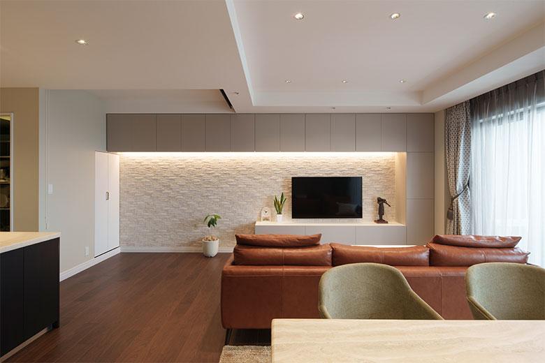 エコカラット貼りの壁に間接照明を使ったリビングでゆったりとした時間を過ごすという。地震に強い家にしたいと壁面収納を設けて物はできるだけしまうようにして、テレビも壁掛けにしたので安心だそう。左奥の天井のくぼみにロールスクリーンが取り付けてあり、息子さんが帰省するとここが寝室となる。