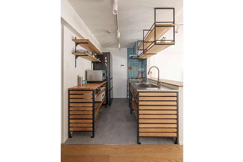 アクセントウォールのネイビータイルが印象的なキッチン。旦那様も立つ機会が増えることを考えてキッチンの棚はすべてオープンにして、どこに何があるかがひと目で分かるようにした。配管を通すためシンク前に壁が立ち上がったが手元が隠れるのがうれしく、コンセントも付けられて家電が使いやすいそう