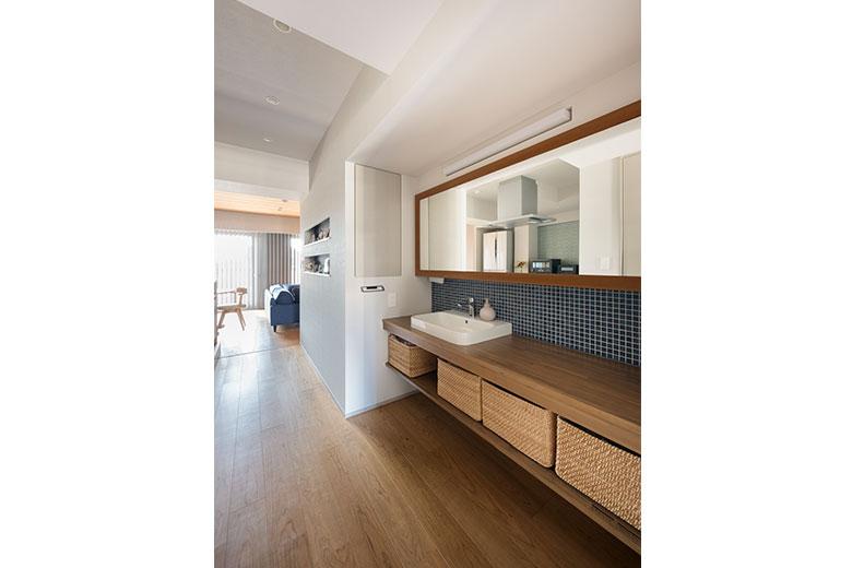 キッチンの前にある廊下洗面。廊下が広くなったのに合わせて提案されたそうだが、カッコよさに惹かれて採用したとか。作業台が広く取られ、大きな鏡は部屋をさらに広く見せる役目も担っている。木目と白の洗面ボウルに、紺色のタイルをアクセントとして使い、清潔感のある仕上がりに