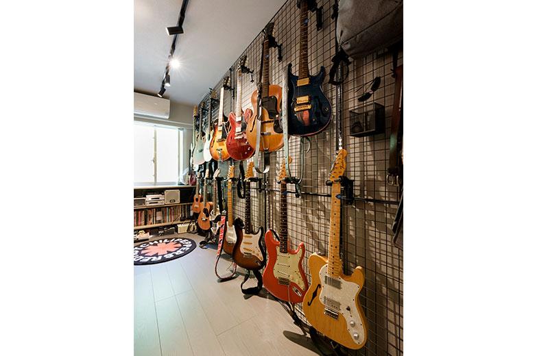 音楽好きの旦那様が楽しむギターは楽器店で見かけた方法をヒントに、ディスプレイネットにハンガーを取り付けて壁面に整然と並べた。「コレクションしているギターの収納方法に困っていましたが、楽器店を訪れて、これだ！と思いました」本やCDは天井までの本棚に収納。この部屋はスイッチやコンセントカバーも黒で統一。