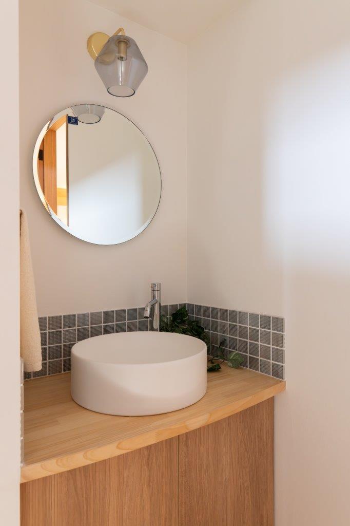 シンプルな中に上質さが光る、洗練された造作洗面スペース。
丸いミラーとやわらかな照明が、空間に優しい印象を与えています。

木のカウンターとキャビネットが温もりを添え、白を基調とした壁とのコントラストが美しく調和。