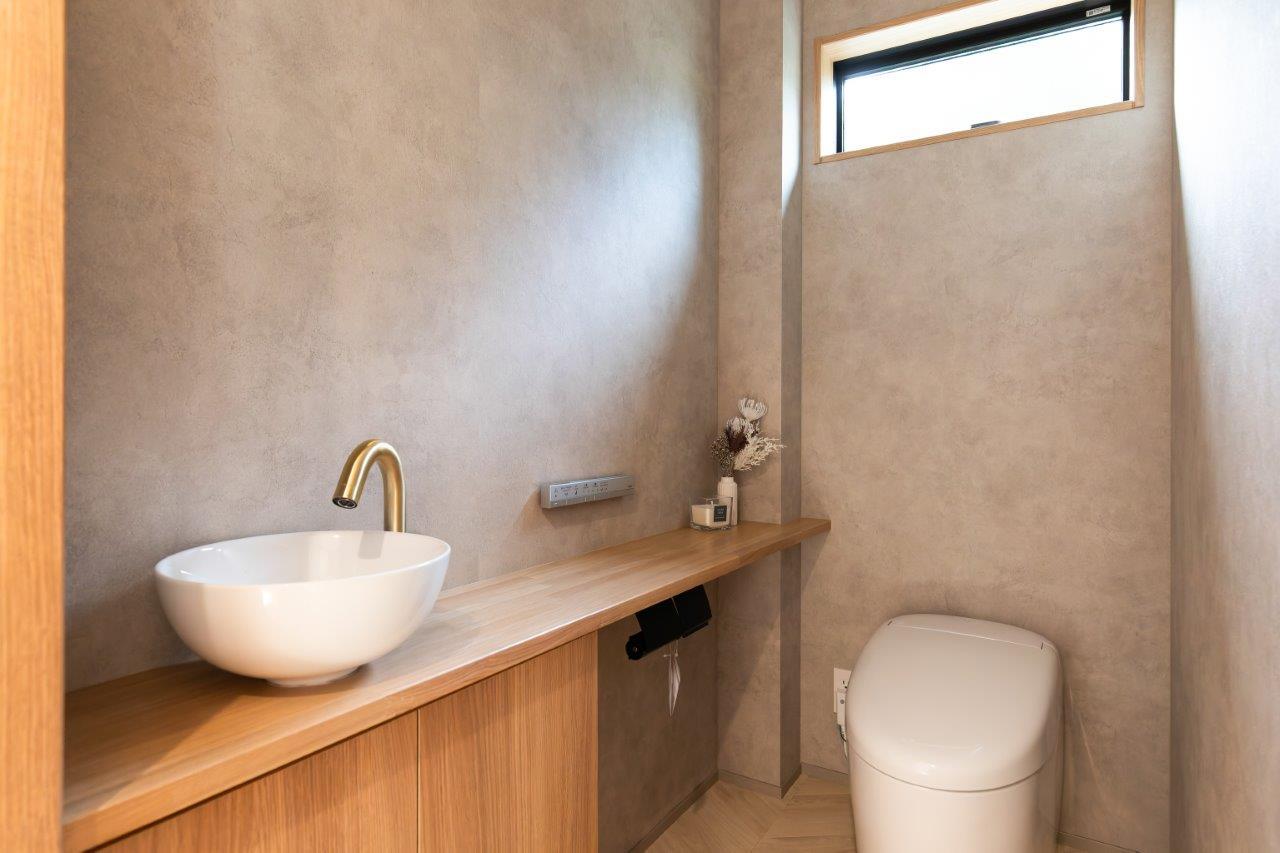落ち着いた質感の壁と木のカウンターが調和した、上質なトイレ空間。手洗いボウルを設け、機能性とデザイン性を兼ね備えた快適な一室です。